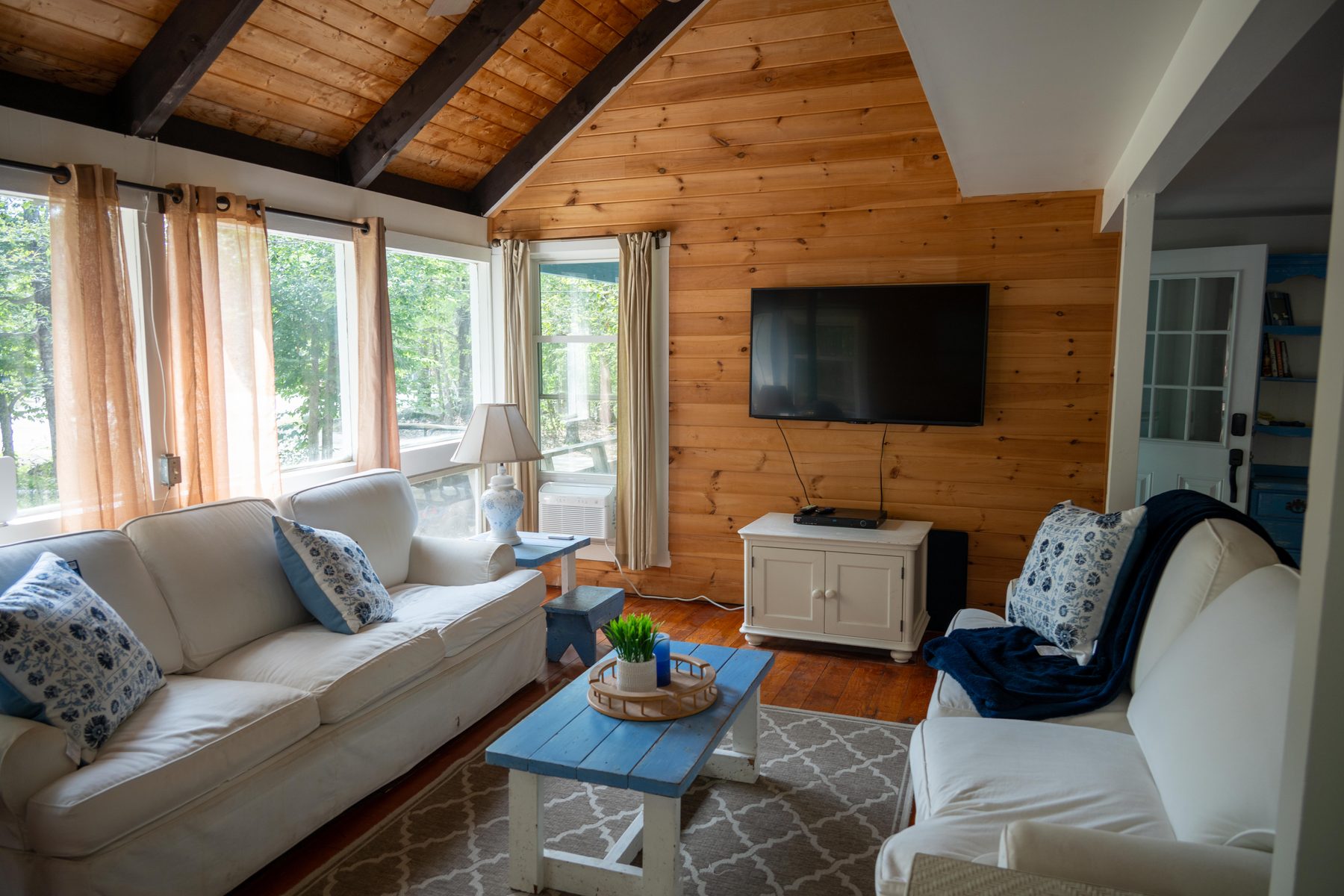 Living room with cathedral pine ceiling, white sofas, and a wall of windows